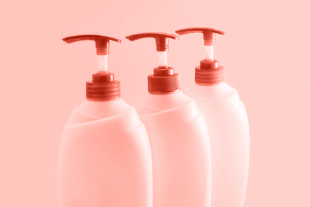 Three plastic bottles with dispenser on coral background. Cosmetics for body and hairの写真素材
