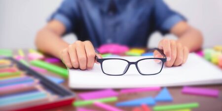 Banner boy holding glasses in their hands. Concept problem of ophthalmology correction of myopia.の写真素材