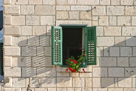 Window with red flowers and green shutters on stone wallの写真素材