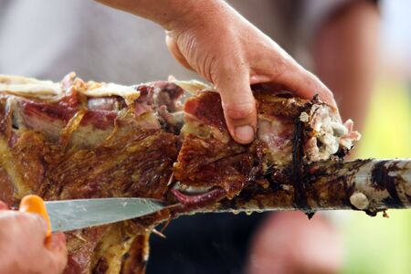 Cutting a leg off the lamb roasted by open fireの写真素材
