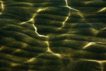 Clear water ripples flowing over yellow patterned sandの写真素材