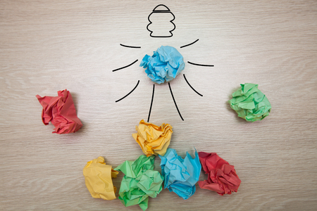 The concept, the idea of colored paper, crumpled drawn light bulb on wooden background for business presentationsの写真素材