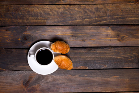 White mug of coffee and a croissant on a wooden background for breakfastの写真素材