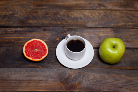 Green fresh apple and coffee in white cup with cut grapefruit on wooden backgroundの写真素材