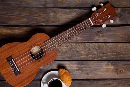 Ukulele ukulele with cup of coffee and croissant on wooden backgroundの写真素材