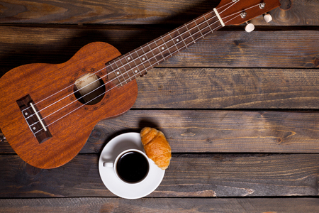 Ukulele ukulele with cup of coffee and croissant on wooden backgroundの写真素材