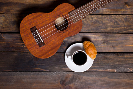 Ukulele ukulele with cup of coffee and croissant on wooden backgroundの写真素材