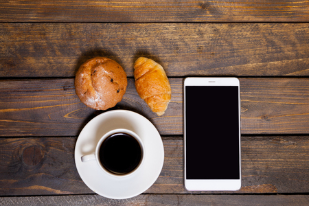 Mobile phone with white mug of coffee and croissants on wooden backgroundの写真素材