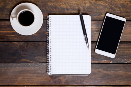 View from above. Mobile phone with white cup of coffee and notepad. Workspace flat lay.の写真素材