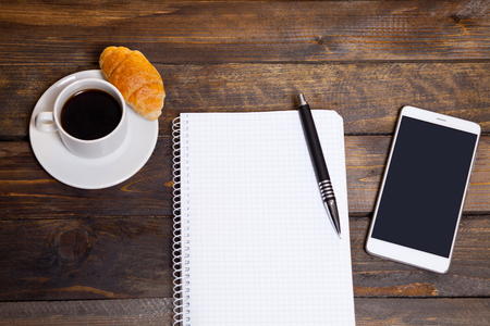 View from above. Mobile phone with white cup of coffee and notepad. Workspace flat lay.の写真素材