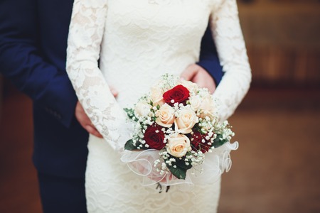 The groom embraces the bride who is holding bouquet, back at the wedding.の写真素材