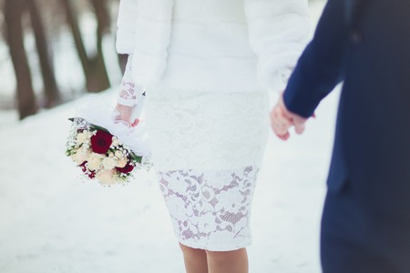 The bride and groom are gently holding hands at the wedding, close-up in the winter.の写真素材