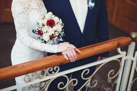 The bride and groom hold hands gently at the wedding, standing on the stairs, close-up.の写真素材