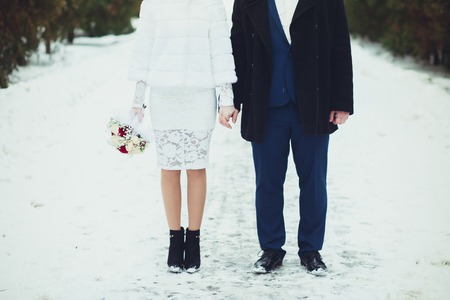 Bride and groom with bouquet to hold gently by the hands at the wedding, close-up in the winter.の写真素材