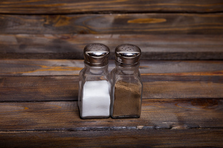 Two transparent cans of salt and pepper shaker on wooden background.の写真素材