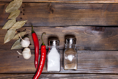 Salt and pepper shaker with bay leaf and red chili pepper, white garlic on background of wood, top view of the workspace.の写真素材