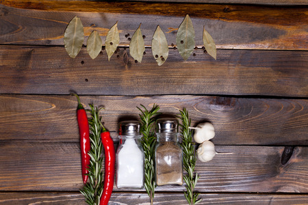Salt and pepper shaker with bay leaf and red chili pepper, white garlic on background of wood, top view of the workspace.の写真素材