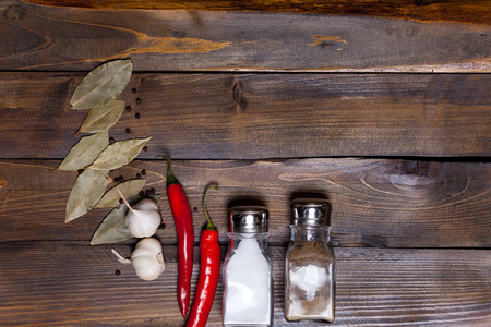 Salt and pepper shaker with bay leaf and red chili pepper, white garlic on background of wood, top view of the workspace.の写真素材