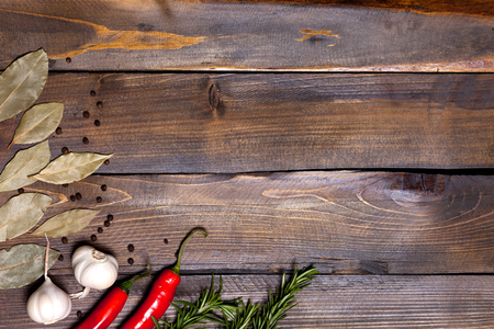 Red chili pepper and rosemary sprigs with laurel leaves and white garlic heads on wooden background.の写真素材