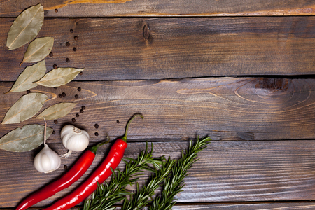 Red chili pepper and rosemary sprigs with laurel leaves and white garlic heads on wooden background.の写真素材