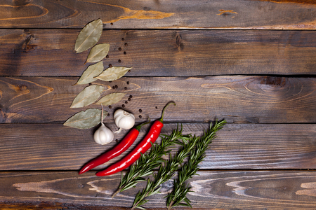 Red chili pepper and rosemary sprigs with laurel leaves and white garlic heads on wooden background.の写真素材