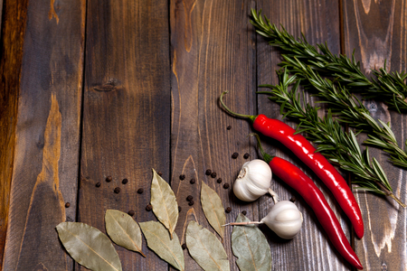 Red chili pepper and rosemary sprigs with laurel leaves and white garlic heads on wooden background.の写真素材
