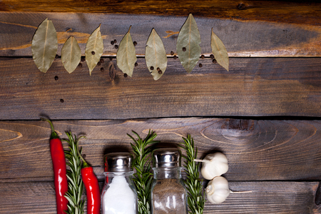 Salt and pepper shaker with bay leaf and red chili pepper, white garlic on background of wood, top view of the workspace.の写真素材