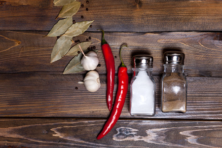 Salt and pepper shaker with bay leaf and red chili pepper, white garlic on background of wood, top view of the workspace.の写真素材