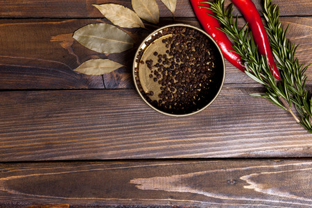 Red chili pepper and rosemary sprigs with laurel leaves and pepper black peas in a jar on wooden background. Top view of the workplace.の写真素材