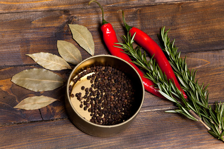 Red chili pepper and rosemary sprigs with laurel leaves and pepper black peas in a jar on wooden background. Top view of the workplace.の写真素材