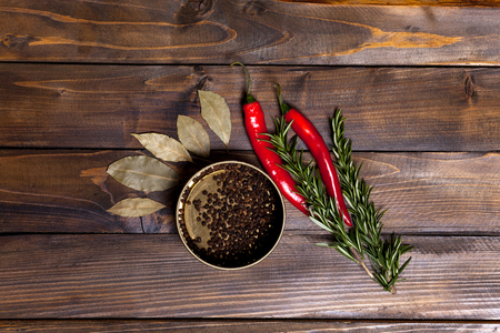 Red chili pepper and rosemary sprigs with laurel leaves and pepper black peas in a jar on wooden background. Top view of the workplace.の写真素材