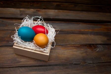 Multi-colored, bright Easter eggs in box with tinsel on wooden background.の写真素材