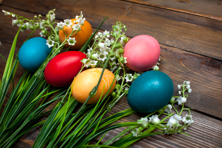 Multi-colored, bright Easter eggs with green, spring lilies of the valley on wooden background.の写真素材