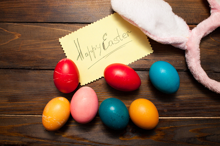 Pink bunny ears with Easter, colored eggs and the words Happy Easter on yellow piece of paper on the background deevyannom as postcards, posters, advertising.の写真素材