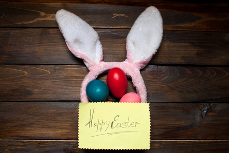 Pink bunny ears with Easter, colored eggs and the words Happy Easter on yellow piece of paper on the background deevyannom as postcards, posters, advertising.の写真素材