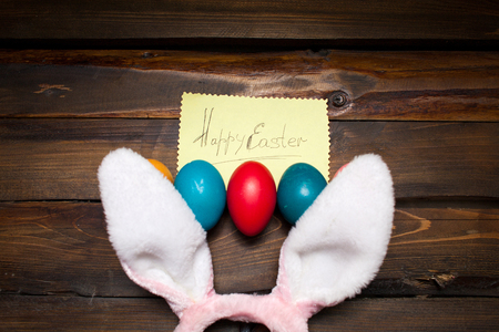 Pink bunny ears with Easter, colored eggs and the words Happy Easter on yellow piece of paper on the background deevyannom as postcards, posters, advertising.の写真素材