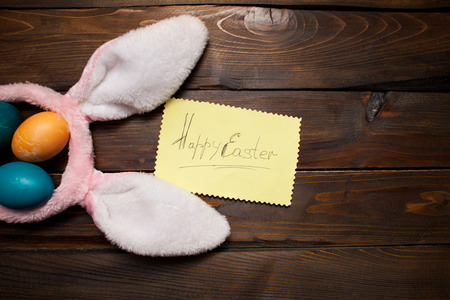 Pink bunny ears with Easter, colored eggs and the words Happy Easter on yellow piece of paper on the background deevyannom as postcards, posters, advertising.の写真素材