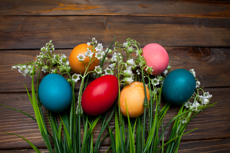 Multi-colored, bright Easter eggs with green, spring lilies of the valley on wooden background.の写真素材