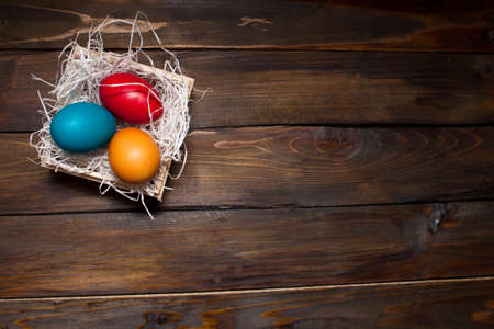 Multi-colored, bright Easter eggs in box with tinsel on wooden background.の写真素材