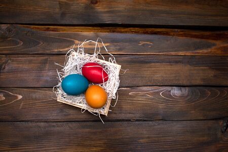 Multi-colored, bright Easter eggs in box with tinsel on wooden background.の写真素材