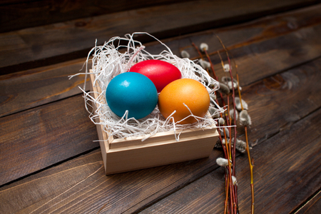 Closed, painted in different bright colors chicken eggs for the holiday Easter in a box on a natural wooden background with willow branches.の写真素材