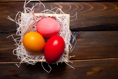 Multi-colored, bright Easter eggs in box with tinsel on wooden background.の写真素材