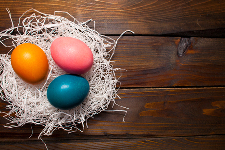Multicolored chicken, dyed eggs for the Easter holiday in the nest on wooden weathering background.の写真素材