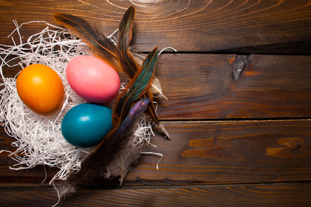 Multicolored chicken, painted eggs for the Easter holiday in nest with feathers on wooden weathering background.の写真素材