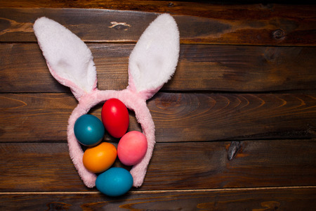 Multicolored chicken, painted eggs for the Easter holiday on a wooden outline background with pink rabbit ears.の写真素材