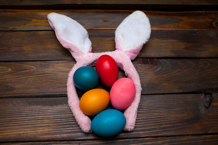Multicolored chicken, painted eggs for the Easter holiday on a wooden outline background with pink rabbit ears.の写真素材