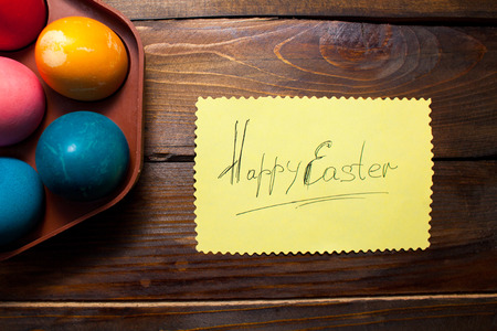 Multicolored chicken, painted eggs for the Easter holiday in box and leaf with the inscription Happy Easter on wooden weathering background.の写真素材