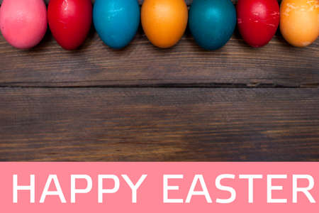 Closed, colored in different bright colors chicken eggs for the holiday Easter on natural wooden background with white text Happy Easter on pink rectangle.の写真素材