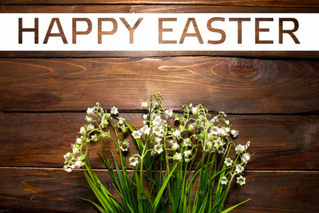 Beautiful spring flowers lily of the valley on woodward wooden background with white rectangle and the text of Happy Easter.の写真素材
