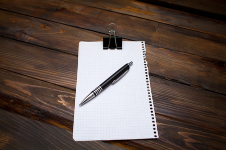 Pen with white sheet of paper in box with clerical clip on wooden background. Top view with copy space.の写真素材